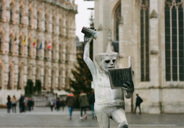 a statue of a man holding a book in front of a building